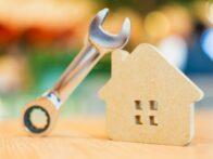 Clé à molette posée contre une maison en bois, illustrant les réparations et l'entretien du logement.