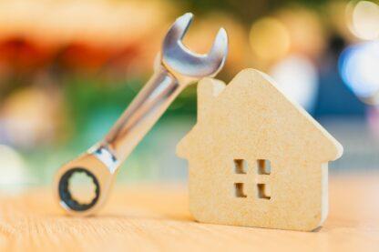 Clé à molette posée contre une maison en bois, illustrant les réparations et l'entretien du logement.