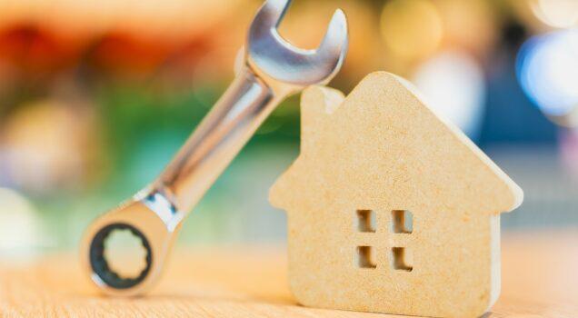 Clé à molette posée contre une maison en bois, illustrant les réparations et l'entretien du logement.